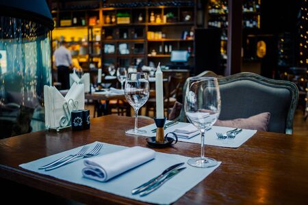 Glasses, flowers, fork, knife served for dinner in restaurant with cozy interior, retro film filter effect.Selective focus.Restaurant interior, modern setting, wine glasses,on textile napkins. Concept banquet.の写真素材