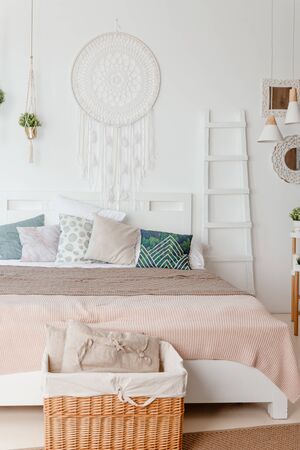 Green, beige pillow on bed in bedroom with pastel colored bedsheets on bed. stylish white apartment design in lagom style.Stylish scandinavian white interior with bed, tropical plant, cozy blanket.の写真素材