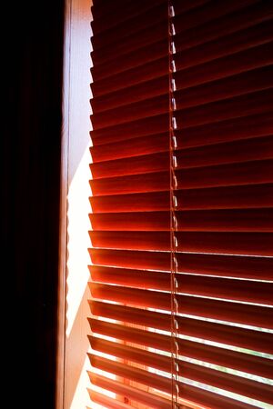 Closed orange plastic blinds with sunlight in the morning. window with blinds. Interior design of living room with window horizontal blinds. Window with Sun-protection jalousieの写真素材