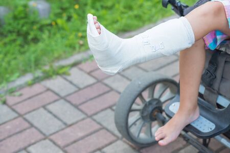 Close up photo of child on wheel chair with cast. Selective focus .copy space. The wheelchair for disability person.child with cast around broken leg in garden.accident concept.の写真素材
