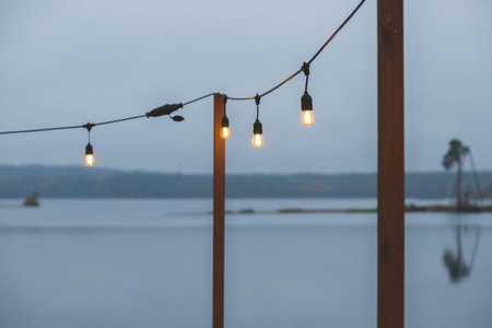 Twilight, gray color sky at the lakescape, electric lamps as garland and wooden terrace, pier....