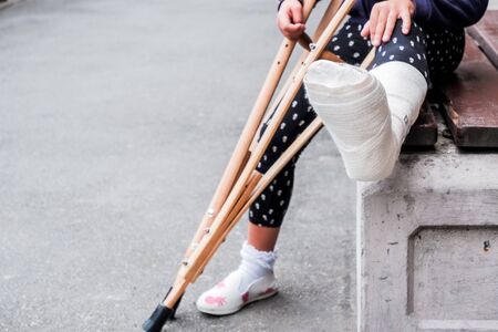 unrecognizable girl sits on the street on a bench with a broken leg and crutches.disabled girl with crutches.an accident while jumping on a trampoline. An ankle fracture.の写真素材