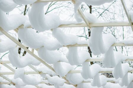 Closeup of wooden deck fence railing side, pole, post covered, in piled, pile of snow after heavy snowing snowstorm, storm at house, home, sunlight. Patio roof after heavy snowfall. Snow pattern.falling snowflakes, snowstorm, storm.の写真素材