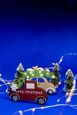 Christmas toy cars with christmas tree on blue background, with garland.New Year holiday background.Christmas tree on wooden car toy with blurred tree background. Christmas holiday celebration, copy space.の写真素材