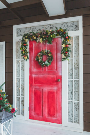 Christmas wreath with red and white berries, stars on wooden red door. beautiful wreath on the front door of a house. Vintage Style. Stylish christmas street decor, Festive decorations and illumination. Winter holidaysの写真素材
