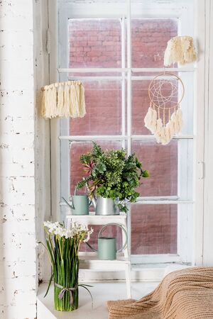 Stylish and modern boho interior of living room with flowers in vase, beige macrame and elegant narcissus, daffodil bouquet. Design home decor. Bohemian concept.cozy apartment.Minimalistic designの写真素材
