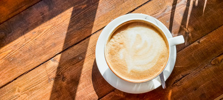 A hot cup of cappuccino coffee with a heart shaped milk foam on a wooden table with a cup of hot tea