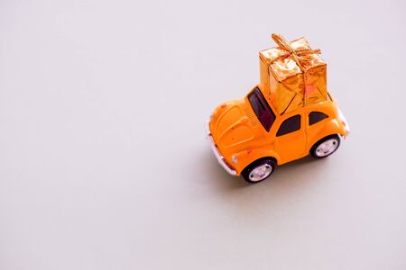 Simply design yellow vintage retro toy car delivering gift box on roof isolated on trendy yellow background. Christmas New Year birthday Valentine s day celebration present romantic concept.の写真素材