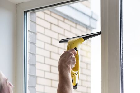 Cleaning windows with electric vacuum cleaner. Spring house cleaning- image.Window washing with a vacuum cleaner.hand with portable professional vacuum cleanerの写真素材