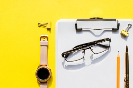Home office workspace mockup with clipboard, watch ,glasses and accessories. check list, empty note paper on yellow background. Office, writer or study concept.Template for blog, bloger, businessの写真素材