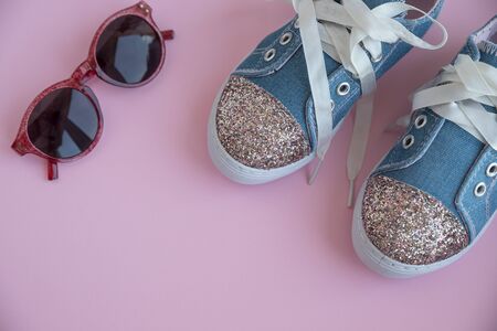 Childs textile lace sneakers. girls shoes on pink background.Fashion kids footwear.Smart casual fashionable denim and shiny shoes.Sunglasses and trendy kids sports shoes.Copy space. Selective focusの写真素材