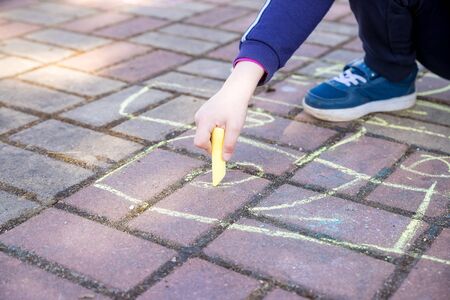 girl sits on concrete asphalt road., on stone pathway. kids painting lines, numbers with chalk on asphalt. selective focus.Little girl hands painting on the pavement using a colorful chalk.の写真素材