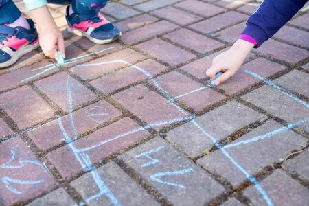 girl sits on concrete asphalt road., on stone pathway. kids painting lines, numbers with chalk on asphalt. selective focus.Little girl hands painting on the pavement using a colorful chalk.の写真素材