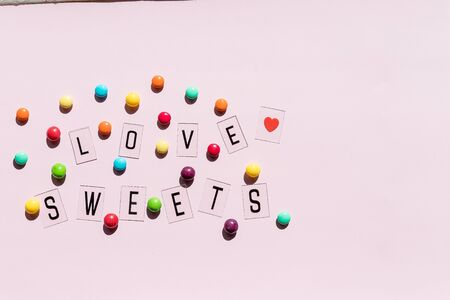 Assortment of sweet candies on pink background.colorful candies and text love sweets.Flat lay composition with jelly beans. Colorful chocolate candies.chocolate buttonsの写真素材