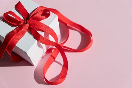 white gift box withred ribbon and bow on yellow background. Copy space.Fashion wrapped square gift or presents box, top view. Flat lay composition for birthday, christmas or wedding.の写真素材