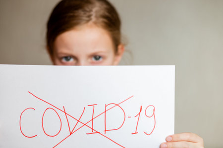 Little girl wearing medical mask and holding white board with text stop coronavirus, COVID-19. SARS, spread around the world. Impact of pandemic virus.の写真素材