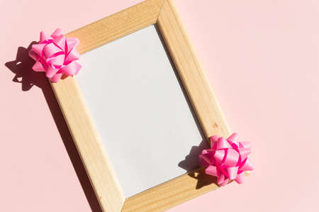 Mock-up of wooden frame with copy space for poster and gift boxes, satin bow on pink background.Pink ribbon bows,Birthday, wedding or Valentines day mock up frame. Holidays greeting cardの写真素材
