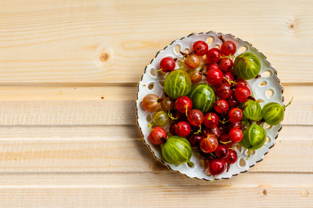 Ripe gooseberry in a glass plate, place for text, top view, summer harvest of berries