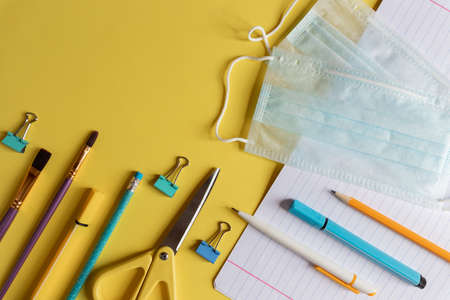 school supplies with medical face mask on yellow background. Protection of schoolchildren and students from the coronavirus covid-19, schooling in a pandemic. Flat lay, top view.post pandemicの写真素材