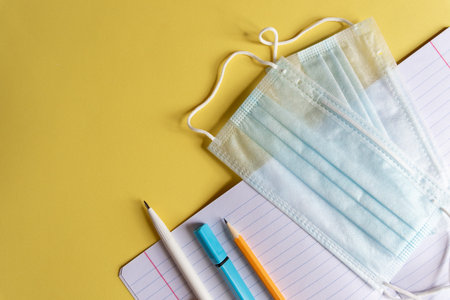 protective mask and school supplies on yellow background, concept of new normality for children and...
