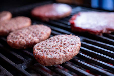 Raw beef burgers with a pinch of salt and black pepper on grill. prepared meat for grilling.Raw burger cutlets. Round patties of raw minced meat roasted on a metal grid.の写真素材