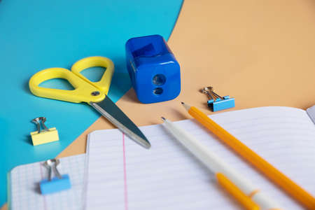 Concept back to school. School stationery. notepad with blank page, pens, pencils, sharpener, paper clips on orange and blue background.Arrangement of various school suppliesの写真素材