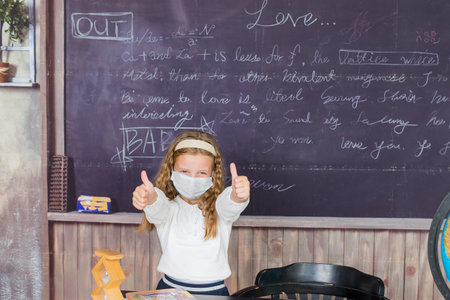 Life during coronavirus pandemic. girl in white blouse with medical protective mask showing thumbs...