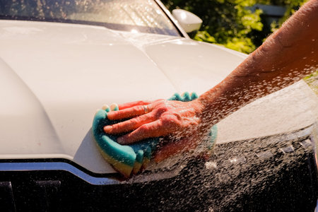 Bwhite car washing on open air.Male hands hold with blue sponge washing car.Soap suds, bubbles and...