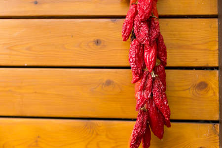 Red chili peppers on the background of the old wooden wall.string of Fresh organic peppers is hanging outside and dry in the sun. dried pepper decoration on wall. The famous Hungarian hot peppers.の写真素材