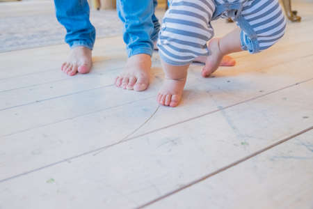 little baby first steps with the help of parents.small and large feet barefoot on the floor, the first steps of the child, learning to walk, family with children.Boy doing first stepsの写真素材