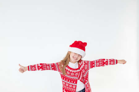 Cute funny santas helper dancing on white background. Christmas holidays concept.New Year celebration. funny baby Santa.beautiful girl wearing red santa hat celebrating christmas day ,having fun.の写真素材