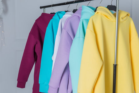 Multicolored hoodies on hangers in a sports store close up, clothing concept. Row of different hoodie ,long sleeve shirts , sweater on hangers.Modern show room selling clothes men, women children.の写真素材