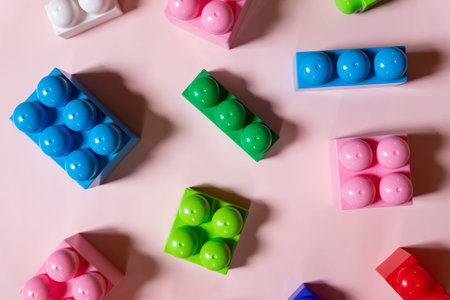 Toys background. Colorful cubes and plastic construction blocks frame on pink background.Kids...