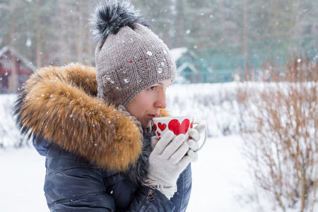 middle age woman holding a cup of hot drink at background of a winter street. outdoor shoot.A girl...