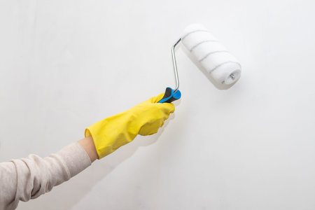 Hand Of Worker In Glove With Paint Roller Painting Wall Inside In Apartment Close Up. Repair In...