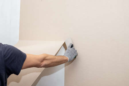 Man hand tear off old light wallpaper from wall.Preparing for home repair work.removing Wallpaper with a spatula, the process of updating the wall room repair. copy spaceの写真素材