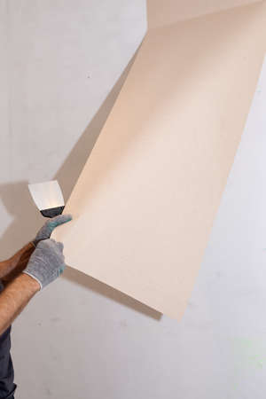 Man hand tear off old light wallpaper from wall.Preparing for home repair work.removing Wallpaper with a spatula, the process of updating the wall room repair. copy spaceの写真素材