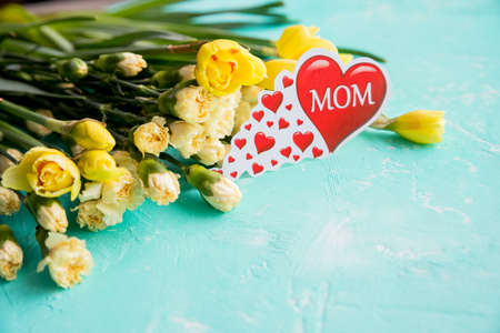 Dear greetings for Mothers Day with a bouquet of yellow daffodils, carnation and red heart with the text MOM ,Happy Mothers Day concept. Postcard with fresh flowers.Copy spaceの写真素材