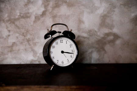 Time Management, Retro black alarm clock alerting at 15 minutes past tree oclock .Business Concept with old alarm clock with a stone background. Selective focus.Copy spaceの写真素材