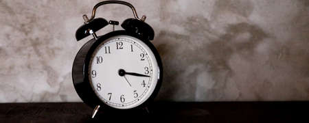 Time Management, Retro black alarm clock alerting at 15 minutes past tree oclock .Business Concept with old alarm clock with a stone background. Selective focus.Copy spaceの写真素材