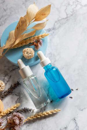 Serum or essential oil in transparent, blue glass bottle with pipette, geometric shapes and dried flowers on marble background. Natural Organic Spa Cosmetic concept.Natural serum for face careの写真素材