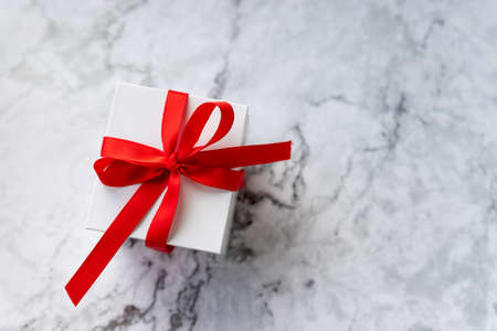 White gift box with red ribbon bow on marble background. holidays and celebration concept. copy space. present for celebrating Christmas, Valentine or an anniversaryの写真素材