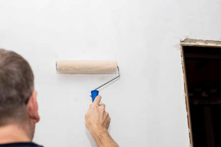 Picture of a hand painting the wall with roller.worker painting wall with paint roller. renovating with white color paint.の写真素材