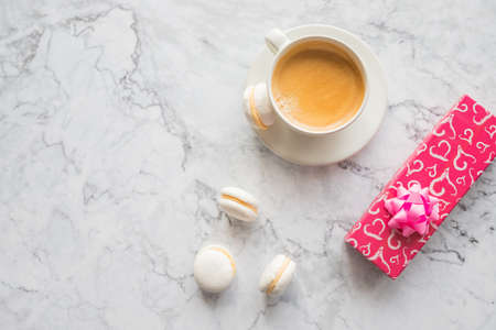 White cup of black coffee with macaroons biscuits .Cozy morning breakfast and present box. Cup of coffee and colorful macaron on marble background top view. Fashion flat lay style. Sweet macaroons.の写真素材