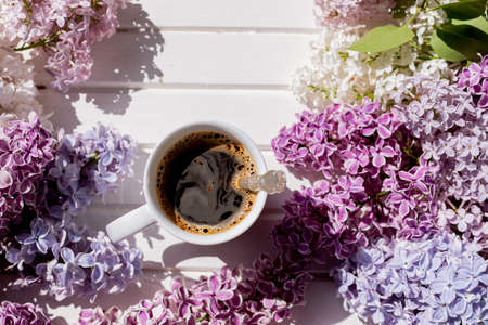 Morning cup of black coffee and branch of blooming purple lilac with green leaves on white background.composition with white cup of coffee,beautiful bouquet of lilacs. concept of spring and comfort.の写真素材