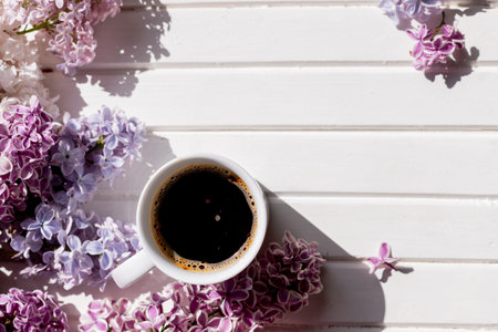 Morning cup of black coffee and branch of blooming purple lilac with green leaves on white...