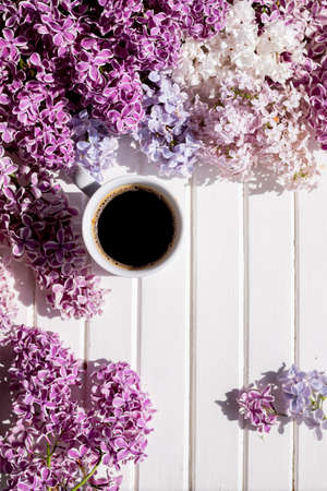 Morning cup of black coffee and branch of blooming purple lilac with green leaves on white background.composition with white cup of coffee,beautiful bouquet of lilacs. concept of spring and comfort.の写真素材