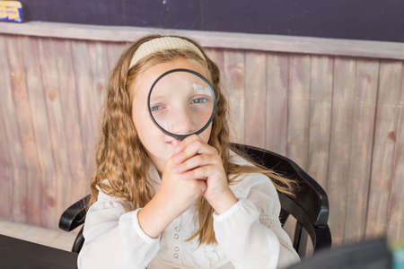 education and school concept - little girl with magnifier at school. schoolgirl sitting in the classroom. Child in an elementary school. Education and learning for kids.の写真素材
