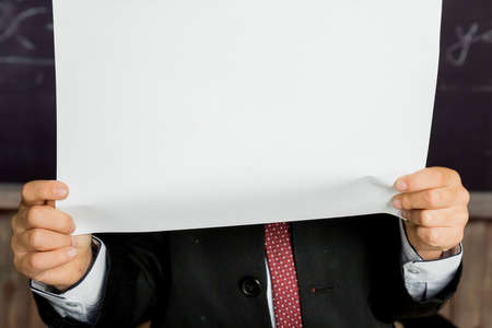 Hands holding blank open notebook over school blackboard. Empty space, school notebook, diary presentation template. boy is behind blank white paper ,advertising board.beginning of the school yearの写真素材