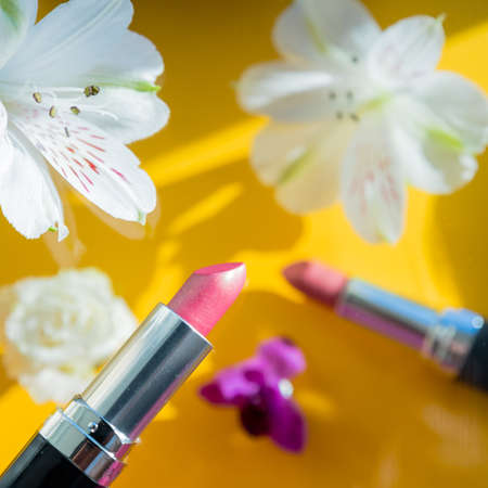 composition with lipstick and flowers on yellow background. Creative flat lay of pink Lipsticks and white alstroemeria frozen in the air. Romantic, beauty concept.decorative makeup productsの写真素材